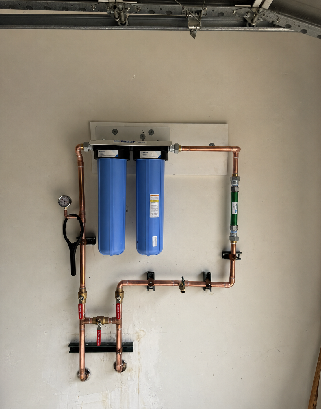 Professionally installed whole home water filtration system with copper piping and dual blue filter cartridges