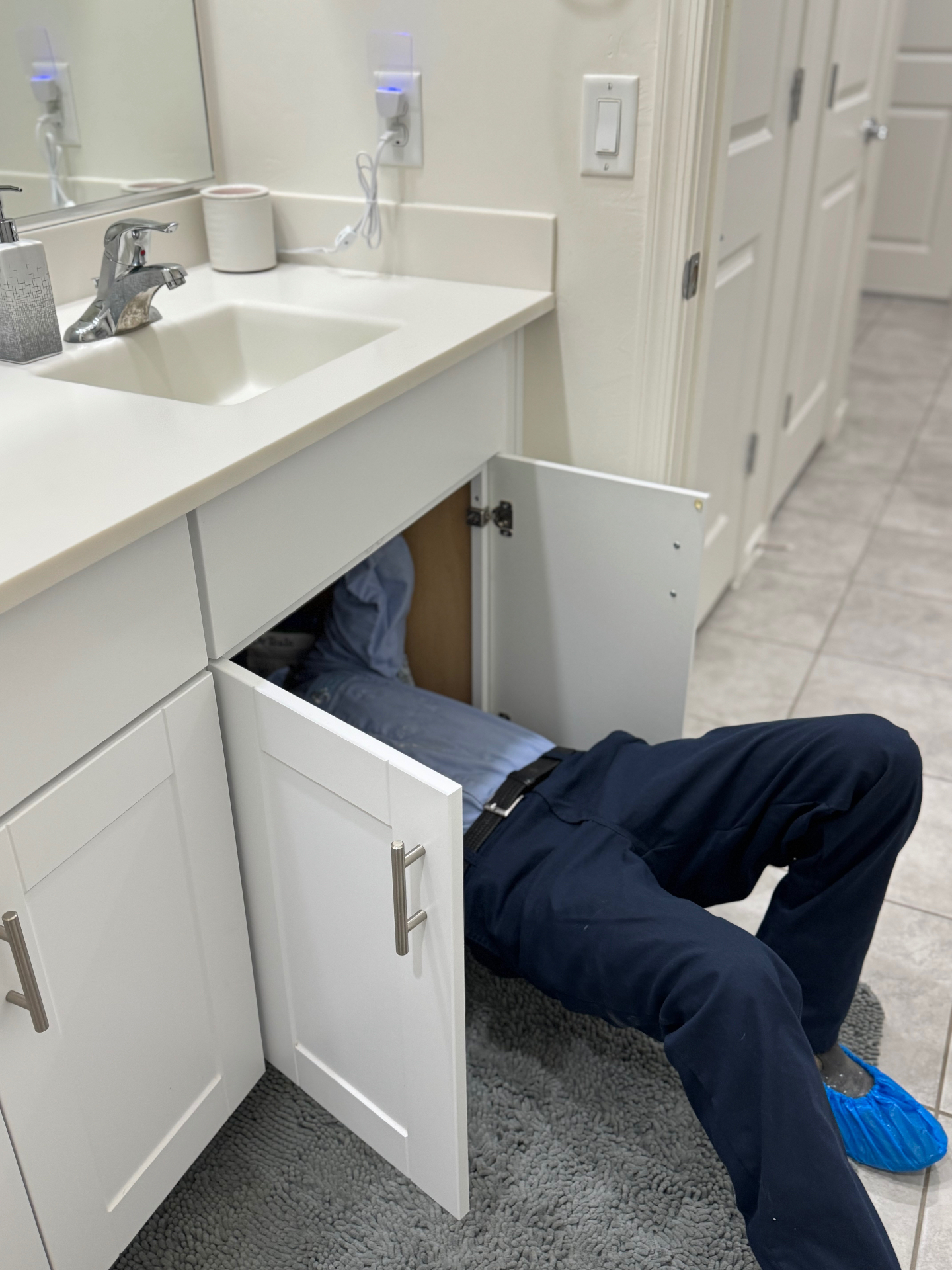 Plumber repairing a leaking bathroom faucet under the sink in Tucson